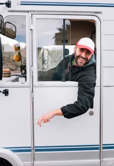 Man smiling and leaning out from the driver's side of a white van.