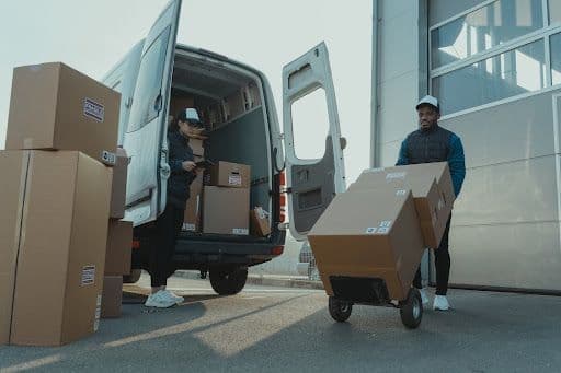 Two people loading cardboard boxes into a van.