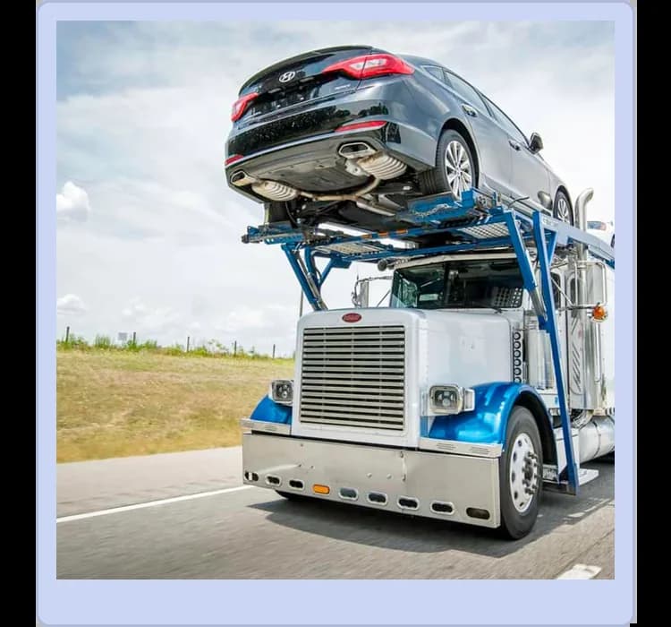 A car carrier truck transports a black sedan on its upper deck while driving on a highway beside grassy fields under a partly cloudy sky.