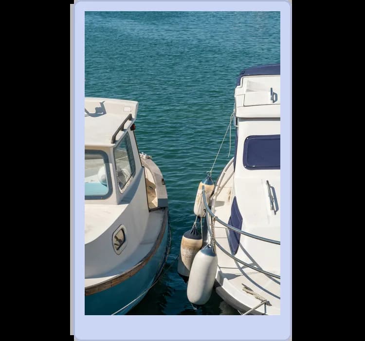Two boats docked side by side on calm blue water, with visible fenders between them to prevent collision damage.