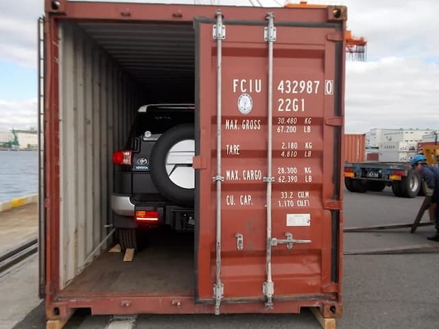 A Toyota SUV is loaded inside a red shipping container with the container door open, showing weight and capacity specifications.