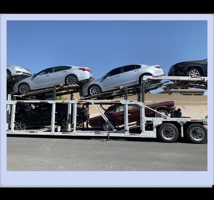 A car carrier trailer loaded with multiple vehicles on two levels is parked by the roadside under a clear sky.