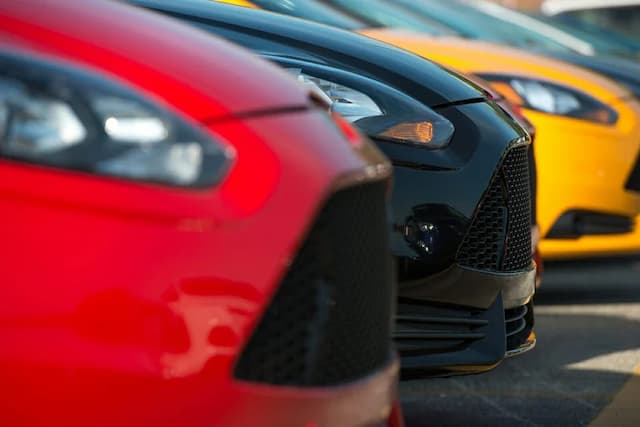 Close-up view of the front ends of several parked cars in red, black, and yellow, arranged in a row.