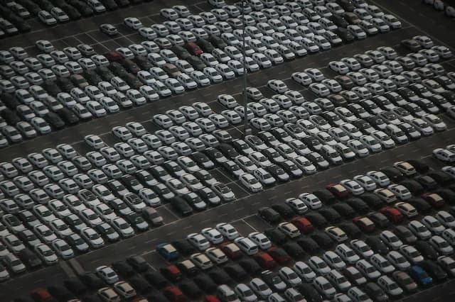 Aerial view of a large parking lot filled mostly with white cars, with a few rows of darker-colored vehicles.