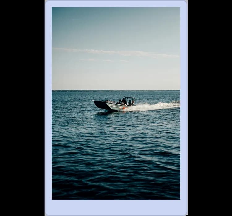 A speedboat moves quickly across a vast, calm body of water under a clear blue sky.