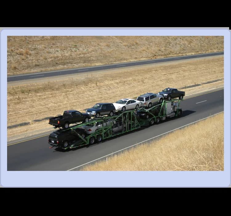 A car carrier truck transports multiple vehicles on a highway, with other cars driving alongside it on a dry, grassy landscape.