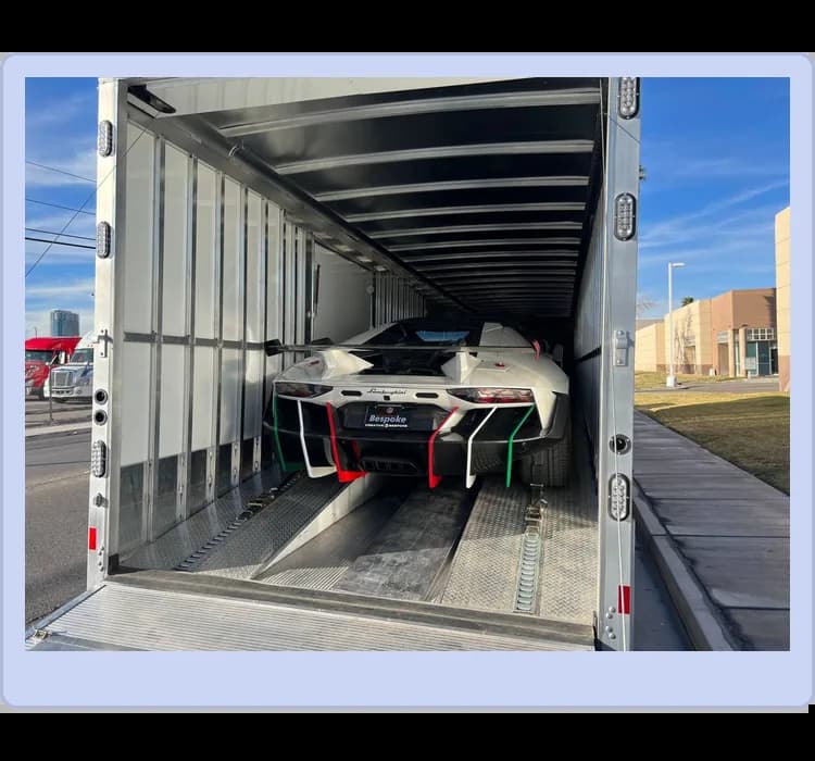 A luxury sports car secured inside an enclosed transport trailer, with the loading ramp down and the rear of the car visible.