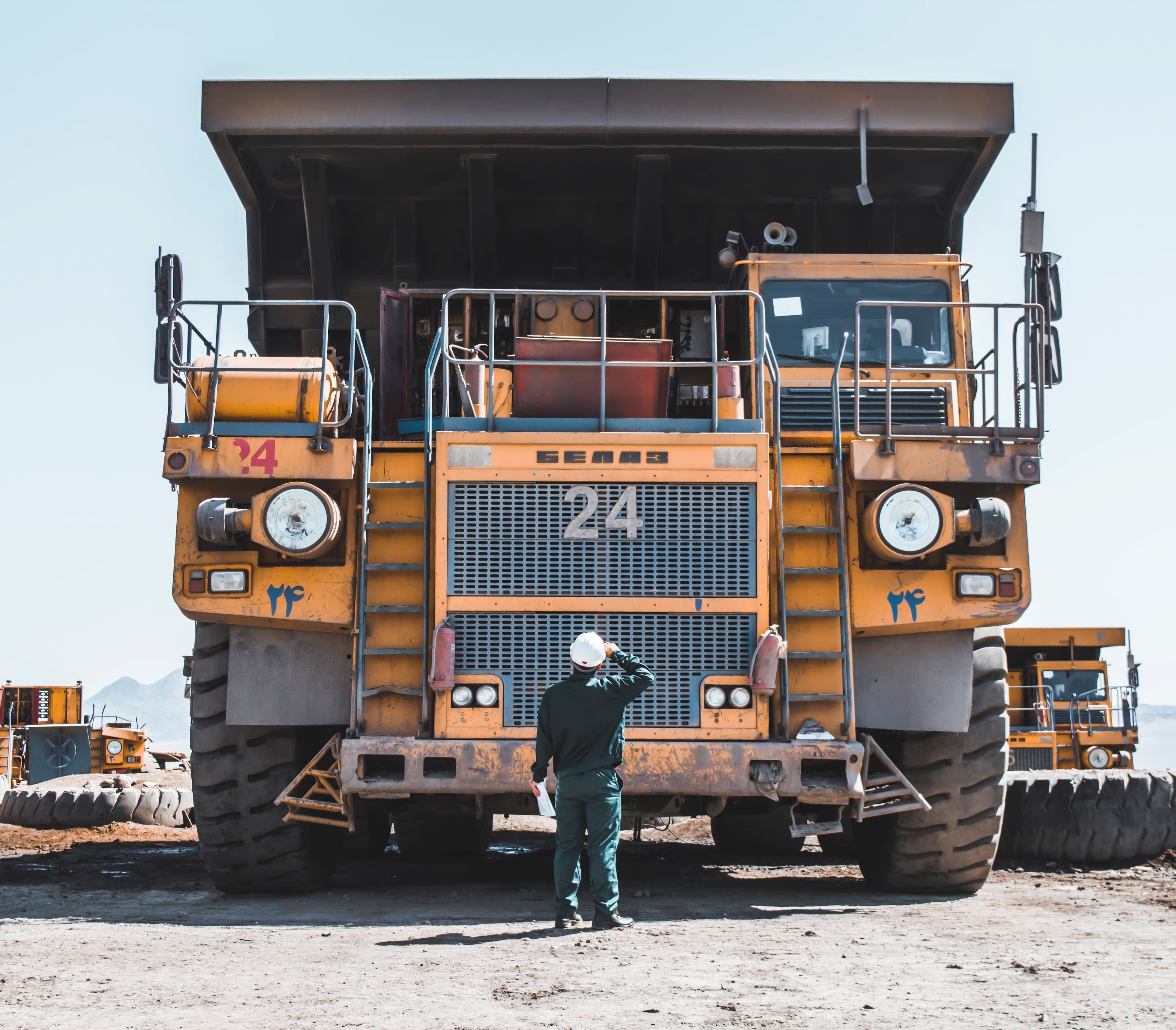A worker standing in front of a large mining dump truck.