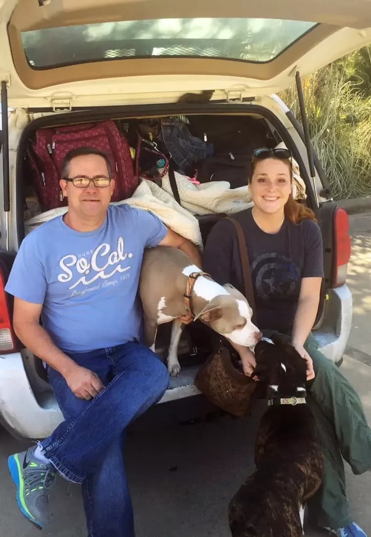 Man and woman sitting in the back of an SUV with two dogs.