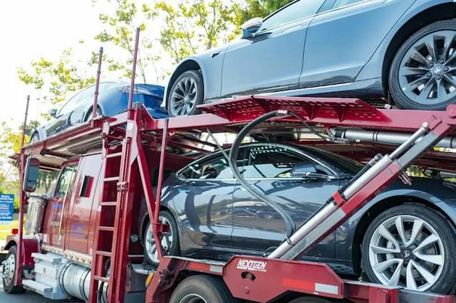 A red car carrier truck loaded with multiple sedans on an outdoor lot during daylight.
