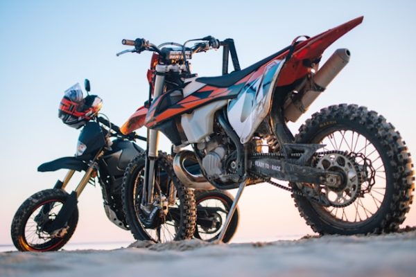 Two dirt bikes, fresh from a dirt bike delivery, are parked on a sandy beach under a clear sky.