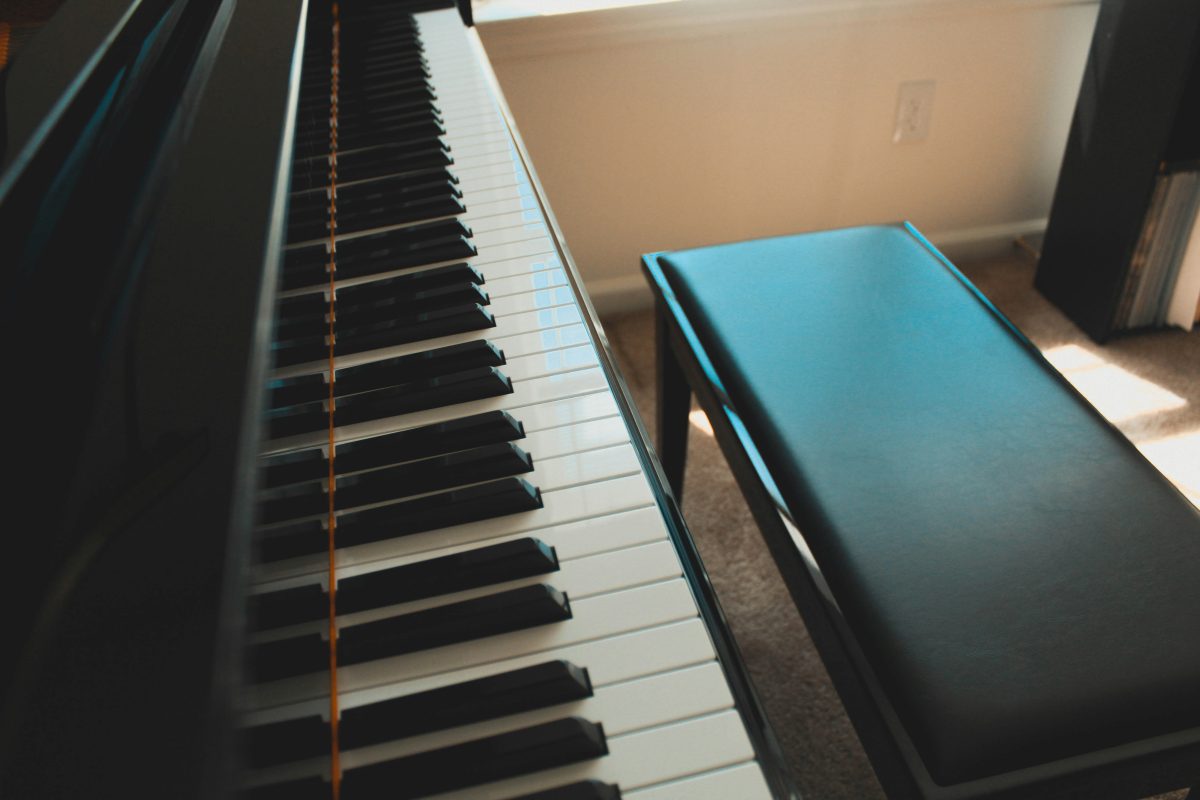 Close-up of a piano keyboard and a black bench in a sunlit room near a window, perfect for those considering piano transportation or careful piano moving.