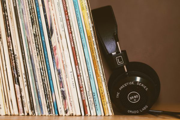A stack of vinyl records stands upright next to a pair of black Grado Labs SR80 Prestige Series headphones resting against them, an ideal setup for those learning how to ship records while keeping their collection safe and stylish.