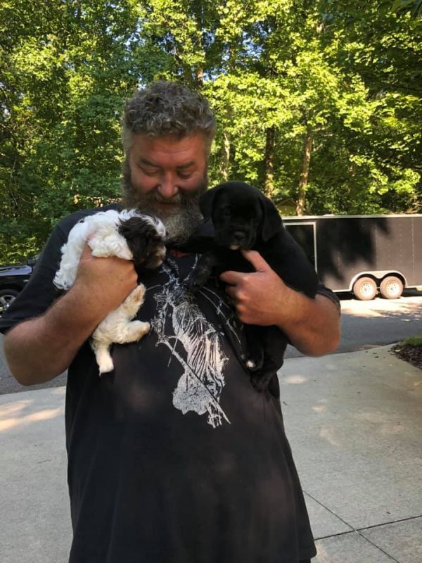 A man cuddling two black puppies.