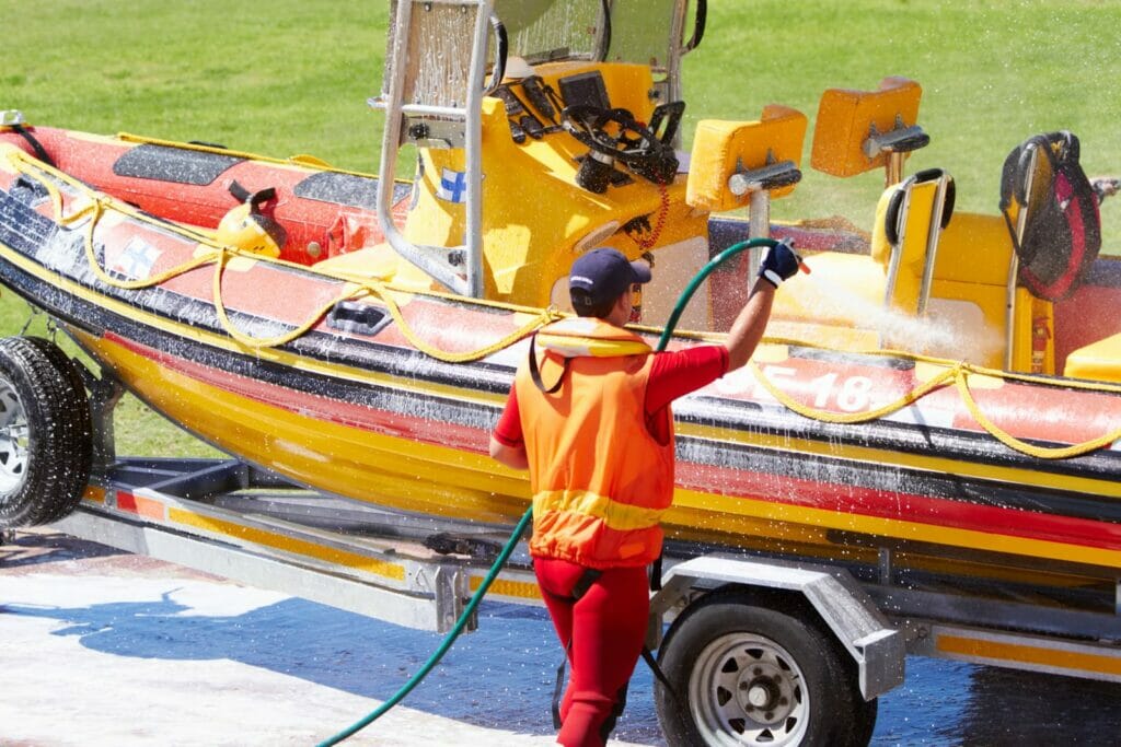 A man is washing a boat using a hose.