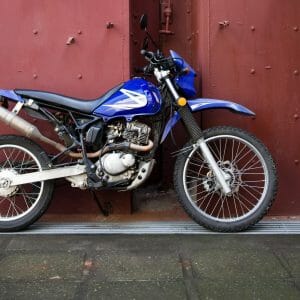 A blue dirt bike parked with motorcycle hitch carriers in front of a red door.
