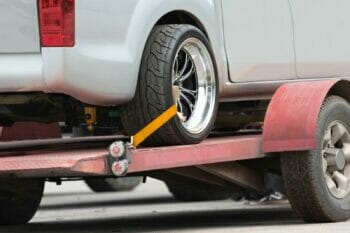A white car being transported on a flatbed truck.