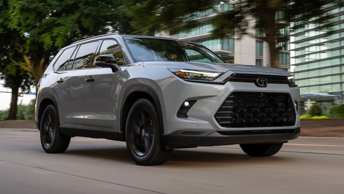 A silver Toyota SUV, one of the best vehicles for transporting dogs, drives on a city street with modern buildings and trees in the background, viewed from a front angle.
