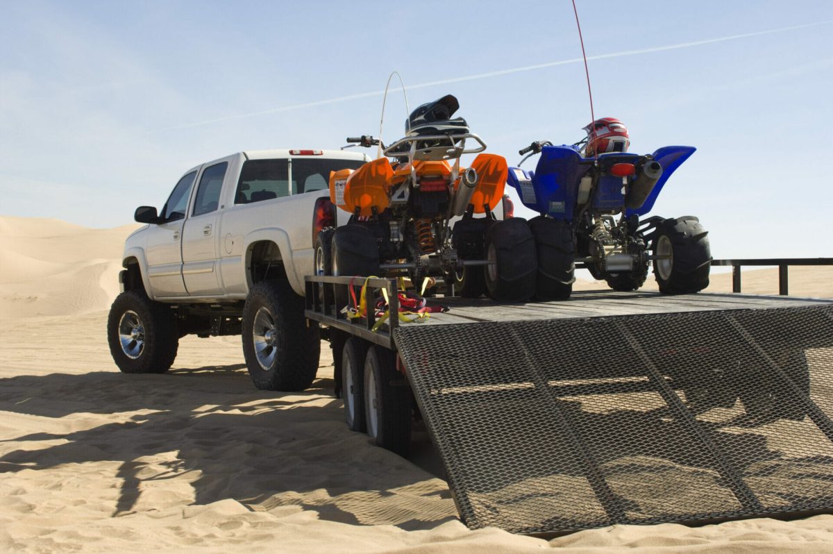 A flatbed truck transporting new vehicles on the sand.