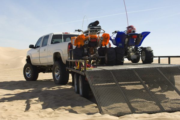 A flatbed truck transporting new vehicles on the sand.