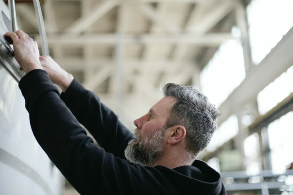 A bearded man performing boat maintenance in a factory.