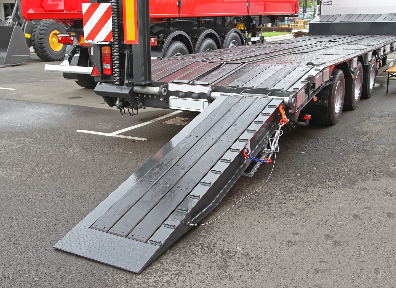 A close-up view of a flatbed trailer with an attached ramp lowered to the ground, showing how to move a boat or heavy equipment easily and safely.