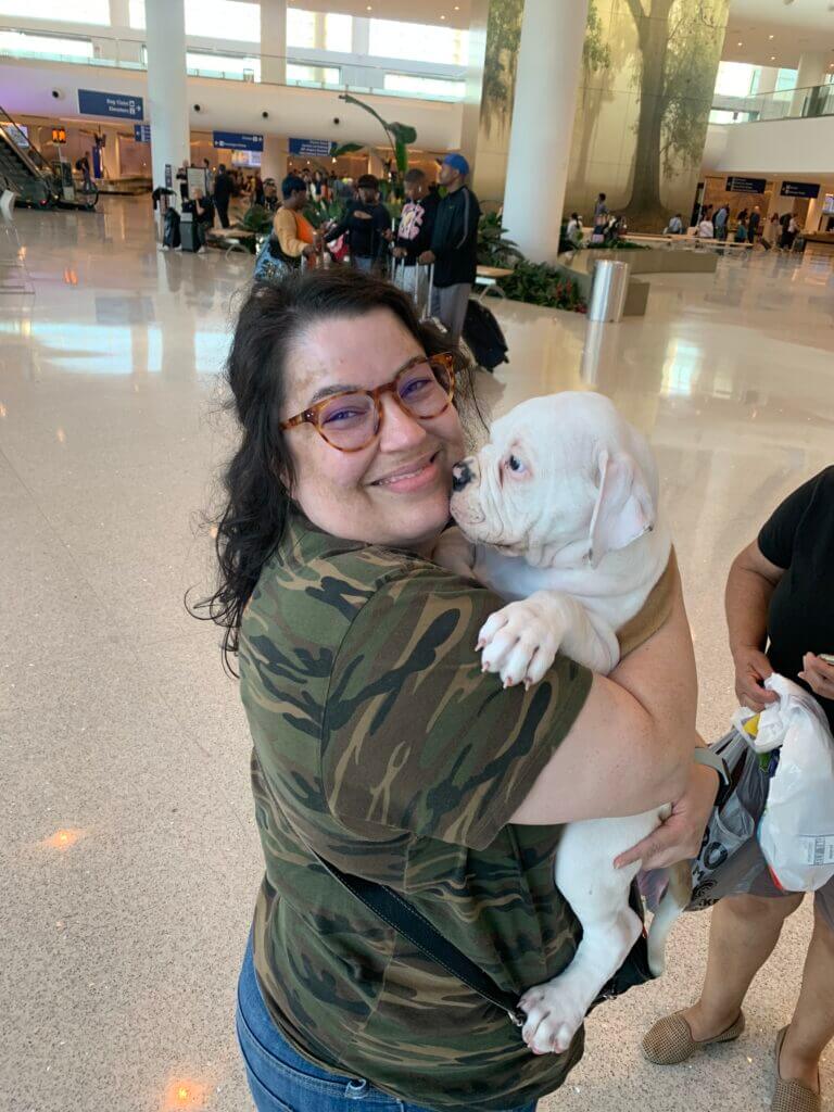A woman holding a white dog in an airport.