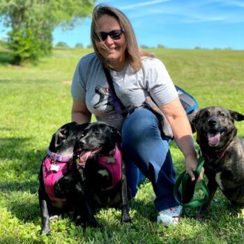 Trista R Teegarden, an animal-loving driver from CitizenShipper, posing with three dogs in a field.