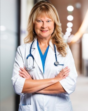 Dr. Neely wearing a white coat and stethoscope, stands with arms crossed and smiles confidently in a brightly lit hallway, ready to provide expert care and advice on pet health.