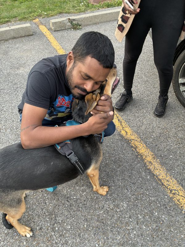 Jon Brouillet kneels in a parking lot, hugging a dog wearing a blue harness during a rescue.